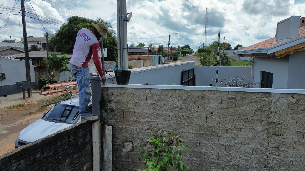Técnico instalando haste de cerca elétrica sobre muro em área urbana